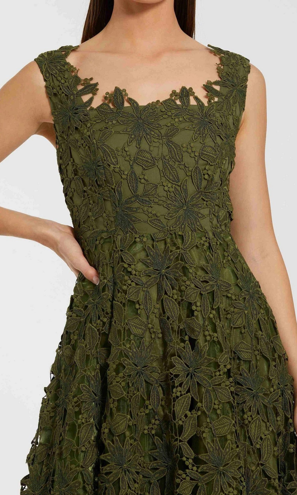 A woman models the Mac Duggal 69073 Midi Party Dress, a sleeveless olive green A-line dress featuring an intricate floral lace overlay; she is posed from shoulder to knee with one hand resting on her hip.